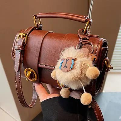 کیف دوشی و دستی وارداتی زنانه مدل رولین چرم عسلی با فرم استوانه ای و آویز پشمی